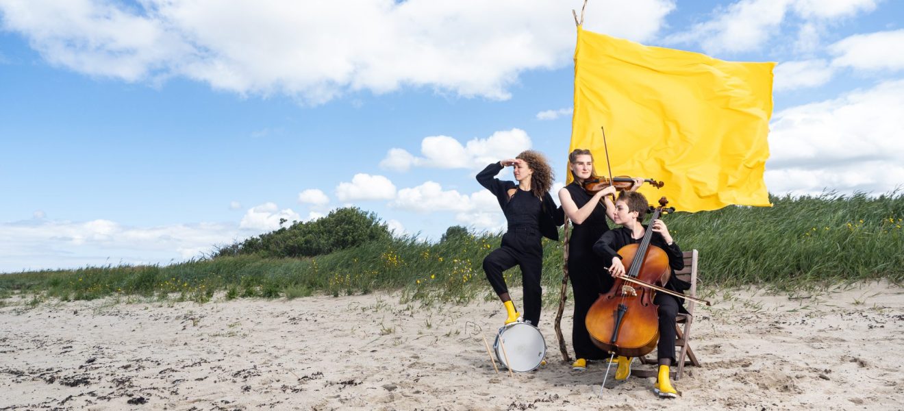 Musikerinnen mit einer gelben Fahne am Strand