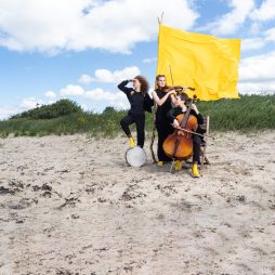 Musikerinnen mit einer gelben Fahne am Strand